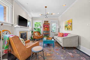 Living area featuring crown molding, plenty of natural light, a chandelier, a glass covered fireplace, and dark wood-style floors