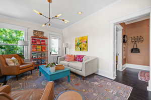 Living area with crown molding, dark wood-style flooring, hanging lights, and plenty of natural light