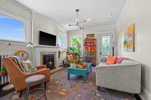 Living room with a warm lit fireplace, a chandelier, and crown molding