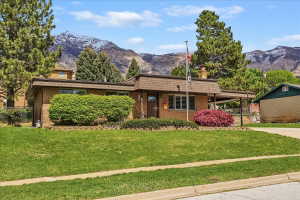 Brick exterior property with an extended covered carport and mature landscaping, set against a mountain backdrop