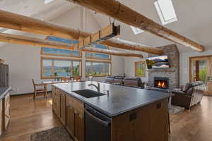 Kitchen with open floor plan, vaulted ceiling, stainless steel dishwasher, a kitchen island with sink, and a stone fireplace