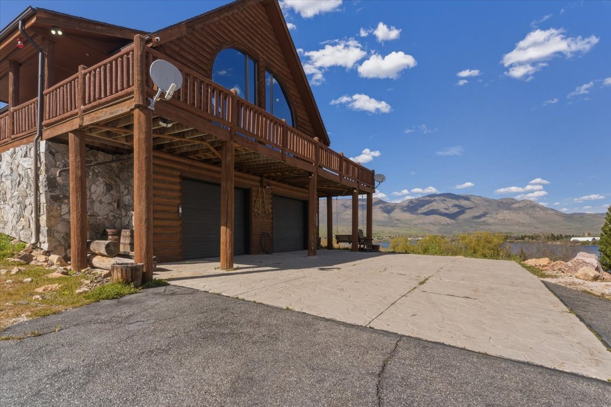 Rear view of house featuring a deck with mountain view, driveway, a garage, stone siding, and log veneer siding
