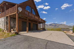 Rear view of house featuring a deck with mountain view, driveway, a garage, stone siding, and log veneer siding