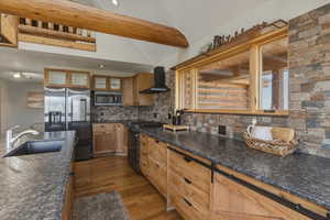 Kitchen featuring stainless steel appliances, glass insert cabinets, vaulted ceiling with beams, dark wood-type flooring, and wood finish cabinetry
