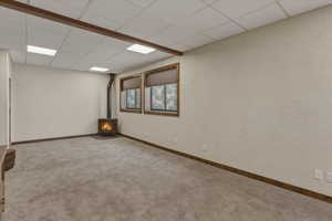 Unfurnished room featuring a drop ceiling, a wood stove, and carpet