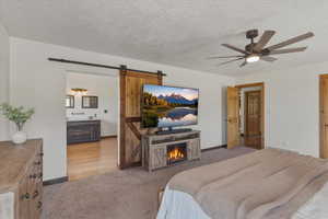 Bedroom featuring light colored carpet, a barn door, a textured ceiling, connected bathroom, and ceiling fan