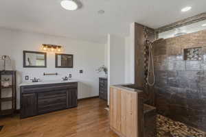 Bathroom with double vanity, walk in shower, dark wood-style floors, and a textured ceiling
