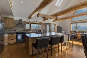 Kitchen featuring a center island with sink, stainless steel appliances, backsplash, wood finish cabinets, and lofted ceiling