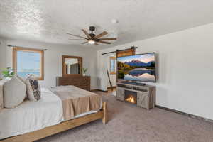 Bedroom featuring carpet, a textured ceiling, ceiling fan, a barn door, and multiple windows