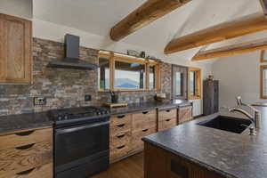 Kitchen featuring black range with gas stovetop, vaulted ceiling with beams, dark wood-style flooring, decorative backsplash, and dark stone counters