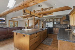 Kitchen with dark countertops, a center island with sink, stainless steel appliances, open floor plan, and ceiling fan