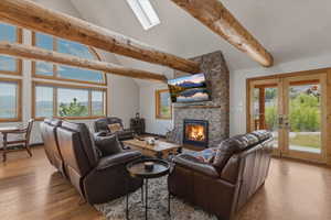 Living room featuring wood finished floors, lofted ceiling, a stone fireplace, a mountain view, and french doors