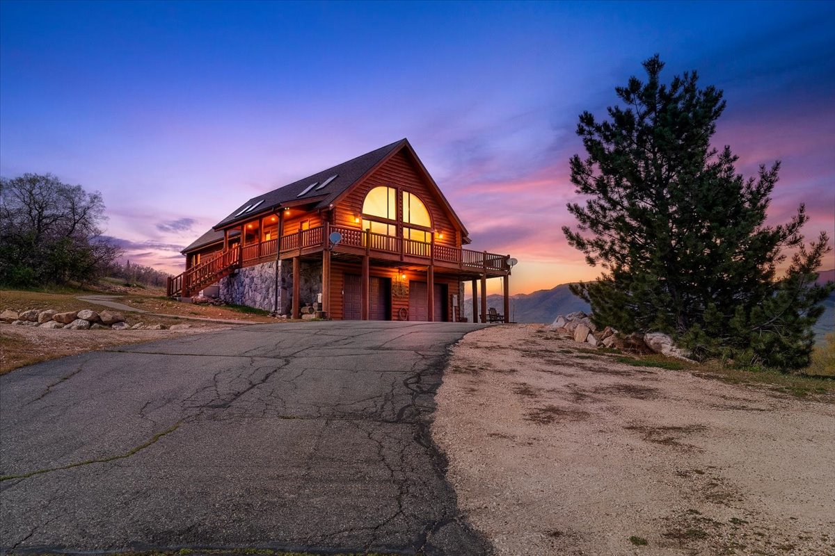 View of front of home with faux log siding, an attached garage, asphalt driveway, a deck, and stone siding