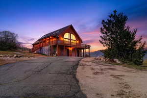 View of front of home with faux log siding, an attached garage, asphalt driveway, a deck, and stone siding