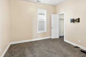 Unfurnished bedroom featuring dark colored carpet and a walk in closet