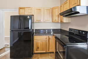 Kitchen featuring black appliances, light wood finish cabinetry, and dark stone counters