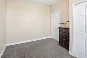Unfurnished bedroom featuring dark colored carpet and baseboards