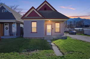 View of front facade with a front yard, a shingled roof, and covered porch