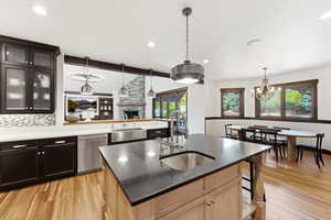 Kitchen with a fireplace, a chandelier, light wood-type flooring, stainless steel dishwasher, and beamed ceiling
