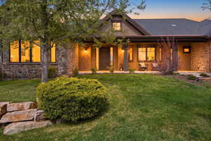 View of front of home with stone siding, a yard, a porch, and roof with shingles