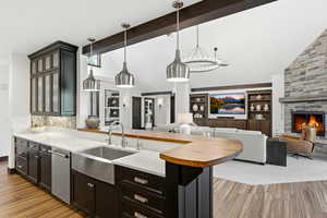 Kitchen featuring lofted ceiling, open floor plan, a fireplace, glass insert cabinets, and a peninsula