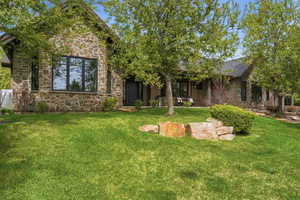 Back of house with stone siding and a lawn