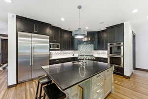 Kitchen featuring built in appliances, an island with sink, a breakfast bar, hanging light fixtures, and dark stone counters