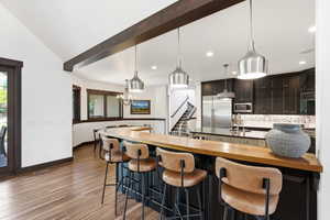 Kitchen with wooden counters, a breakfast bar, a peninsula, decorative backsplash, and vaulted ceiling with beams