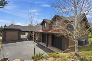View of front facade with a shingled roof, a garage, asphalt driveway, and a storage unit