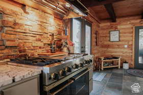 Kitchen featuring range with two ovens, log walls, light stone countertops, and a wood ceiling with exposed beams