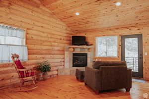 Living area featuring light wood finished floors, a tile fireplace, a vaulted wood ceiling, and rustic walls