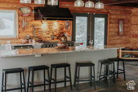Kitchen featuring rustic walls, ventilation hood, a kitchen breakfast bar, light stone counters, and beam ceiling