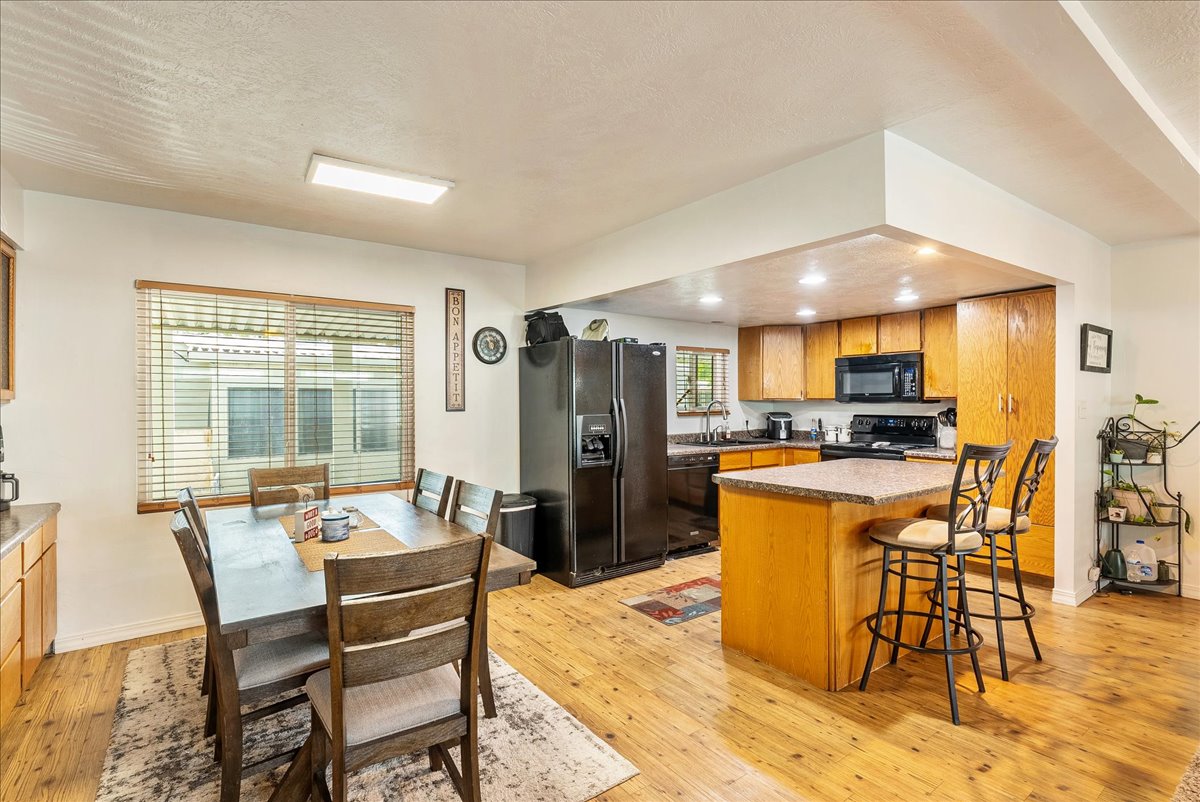 Kitchen with black appliances, light wood-style flooring, a breakfast bar area, wood finish cabinets, and a center island