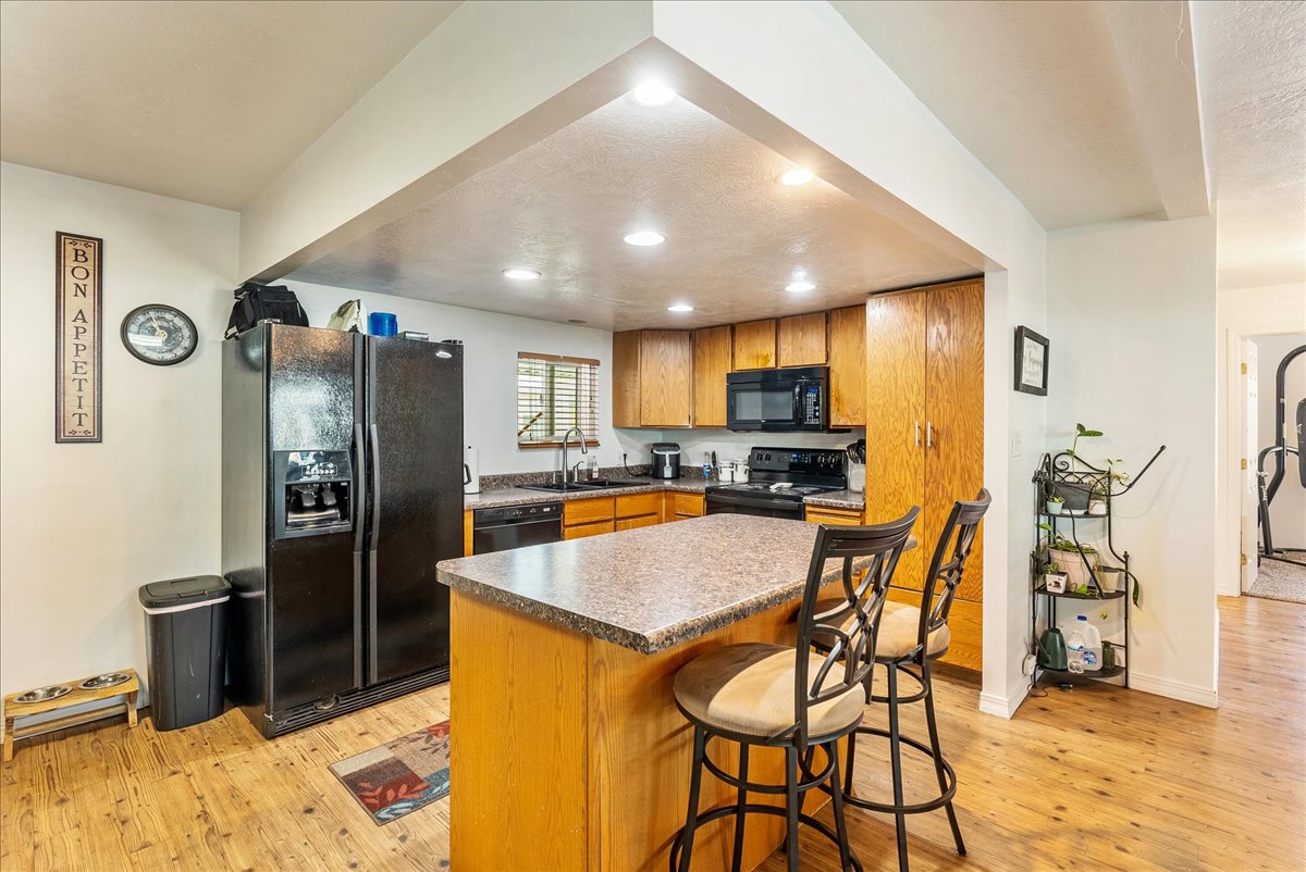 Kitchen featuring a breakfast bar area, black appliances, a center island, light wood finished floors, and recessed lighting