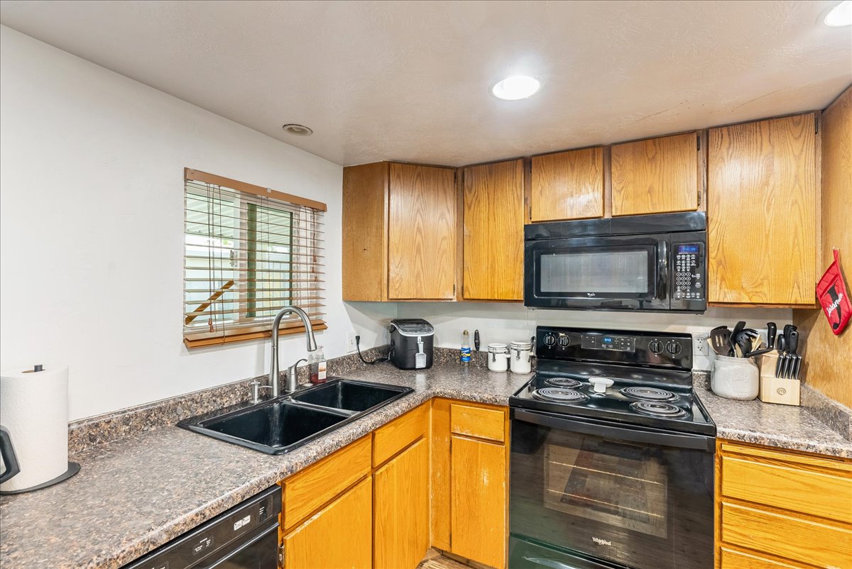 Kitchen featuring black appliances, wood finish cabinetry, dark countertops, and recessed lighting