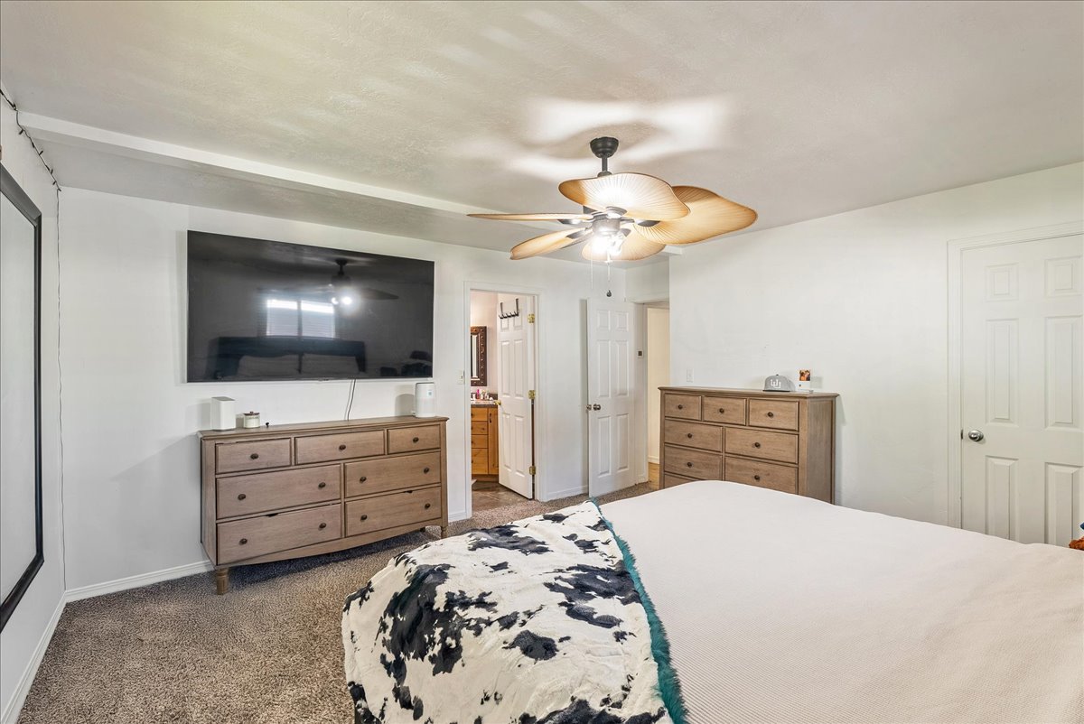 Bedroom with dark colored carpet, a ceiling fan, and ensuite bathroom