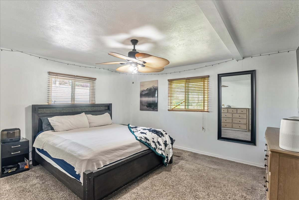 Bedroom featuring a textured ceiling, carpet floors, ceiling fan, and beamed ceiling
