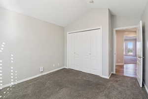 Unfurnished bedroom with dark colored carpet, a closet, and vaulted ceiling
