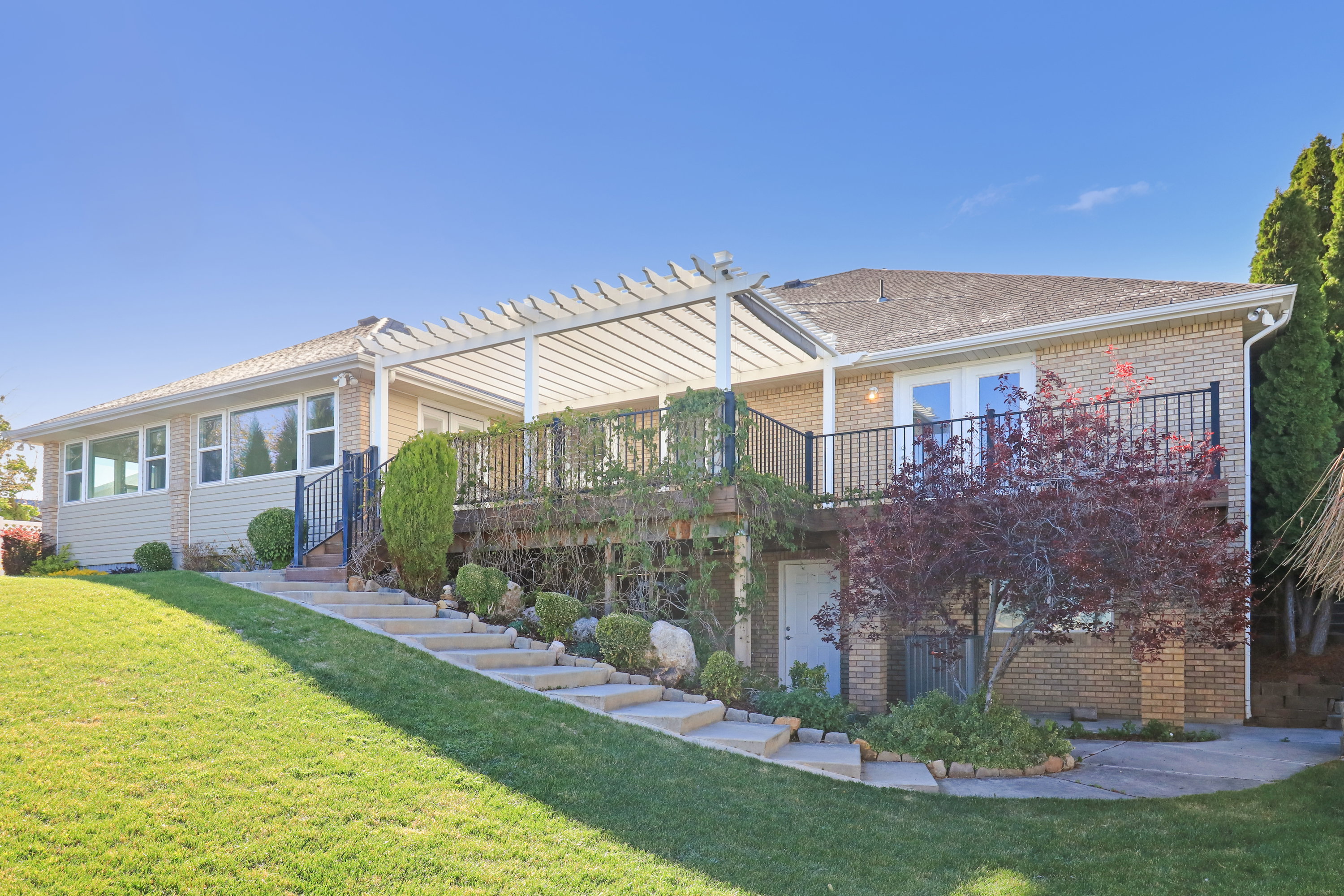 Back of property featuring brick siding, a yard, a deck, and a pergola