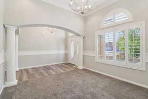 Foyer entrance with ornate columns, suspended lighting, light colored carpet, healthy amount of natural light, and crown molding