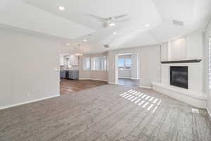 Unfurnished living room with ceiling fan, a brick fireplace, dark colored carpet, suspended lighting, and vaulted ceiling