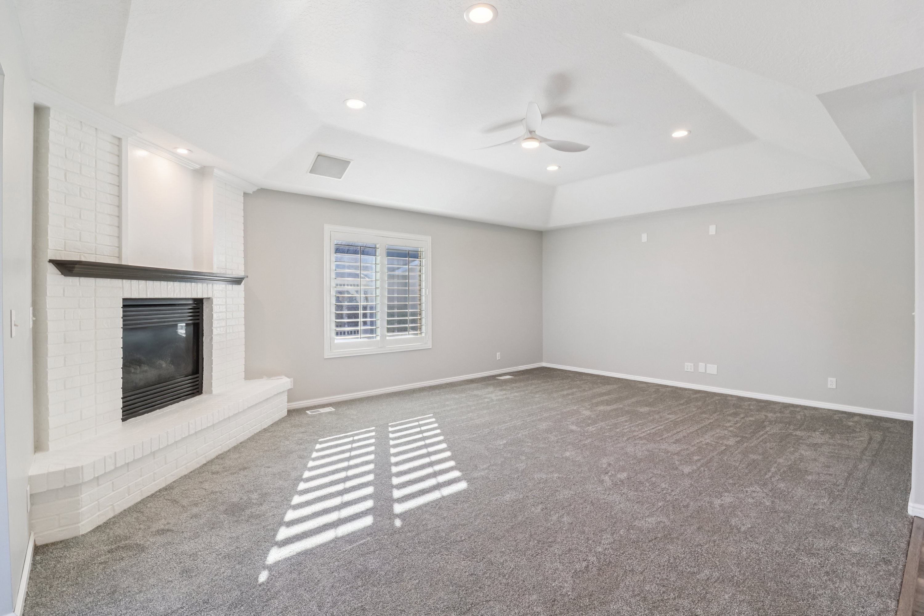 Unfurnished living room featuring dark carpet, a raised ceiling, a fireplace, a ceiling fan, and recessed lighting