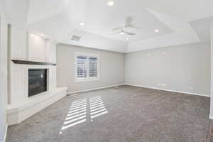 Unfurnished living room featuring dark carpet, a raised ceiling, a fireplace, a ceiling fan, and recessed lighting