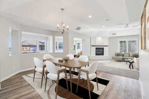 Dining area featuring light wood-type flooring, suspended lighting, a fireplace, and vaulted ceiling