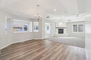 Unfurnished living room featuring hanging lights, a fireplace, light wood-style floors, vaulted ceiling, and ceiling fan