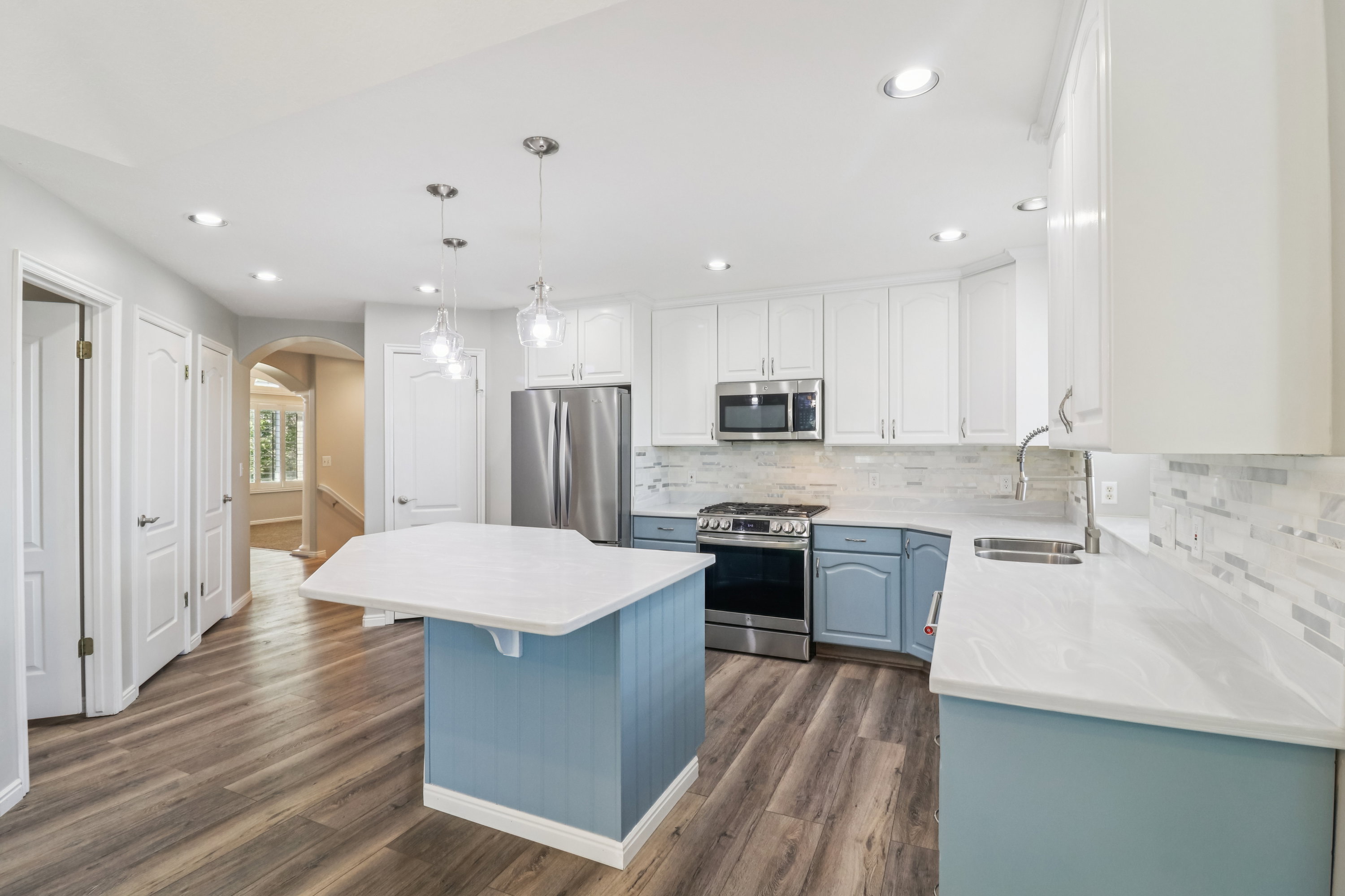 Dual tone kitchen featuring arched walkways, two tone color scheme, stainless steel appliances, a kitchen island, and dark wood-style flooring
