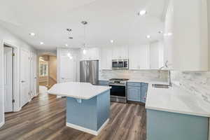 Dual tone kitchen featuring arched walkways, two tone color scheme, stainless steel appliances, a kitchen island, and dark wood-style flooring