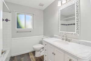Full bathroom with wainscoting, vanity, dark wood-type flooring, and shower / bathtub combination