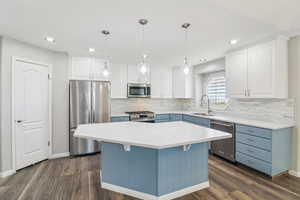 Kitchen featuring two tone cabinets, stainless steel appliances, pendant lighting, a center island, and dark wood-type flooring
