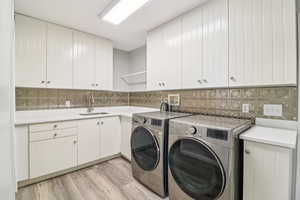 Laundry area with light wood finished floors, washer and dryer, and cabinet space